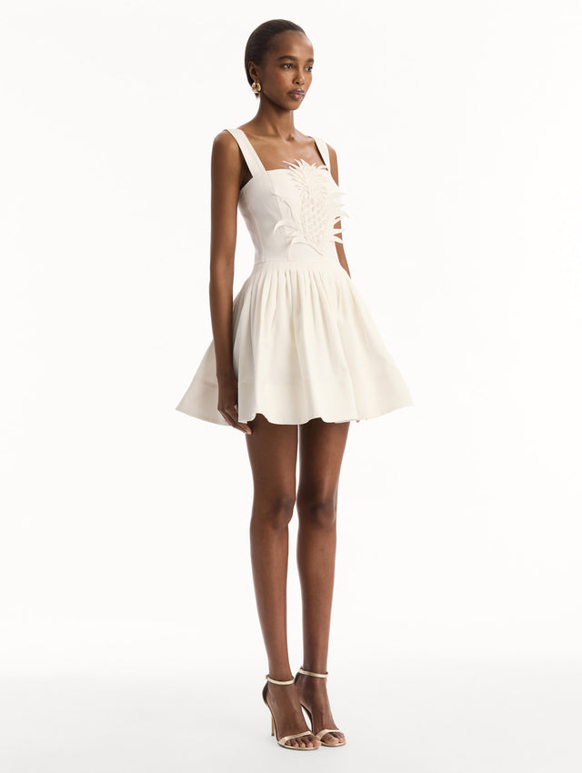 The model is wearing the pineapple appliqué denim dress with a structured bodice in the color white. Side view.