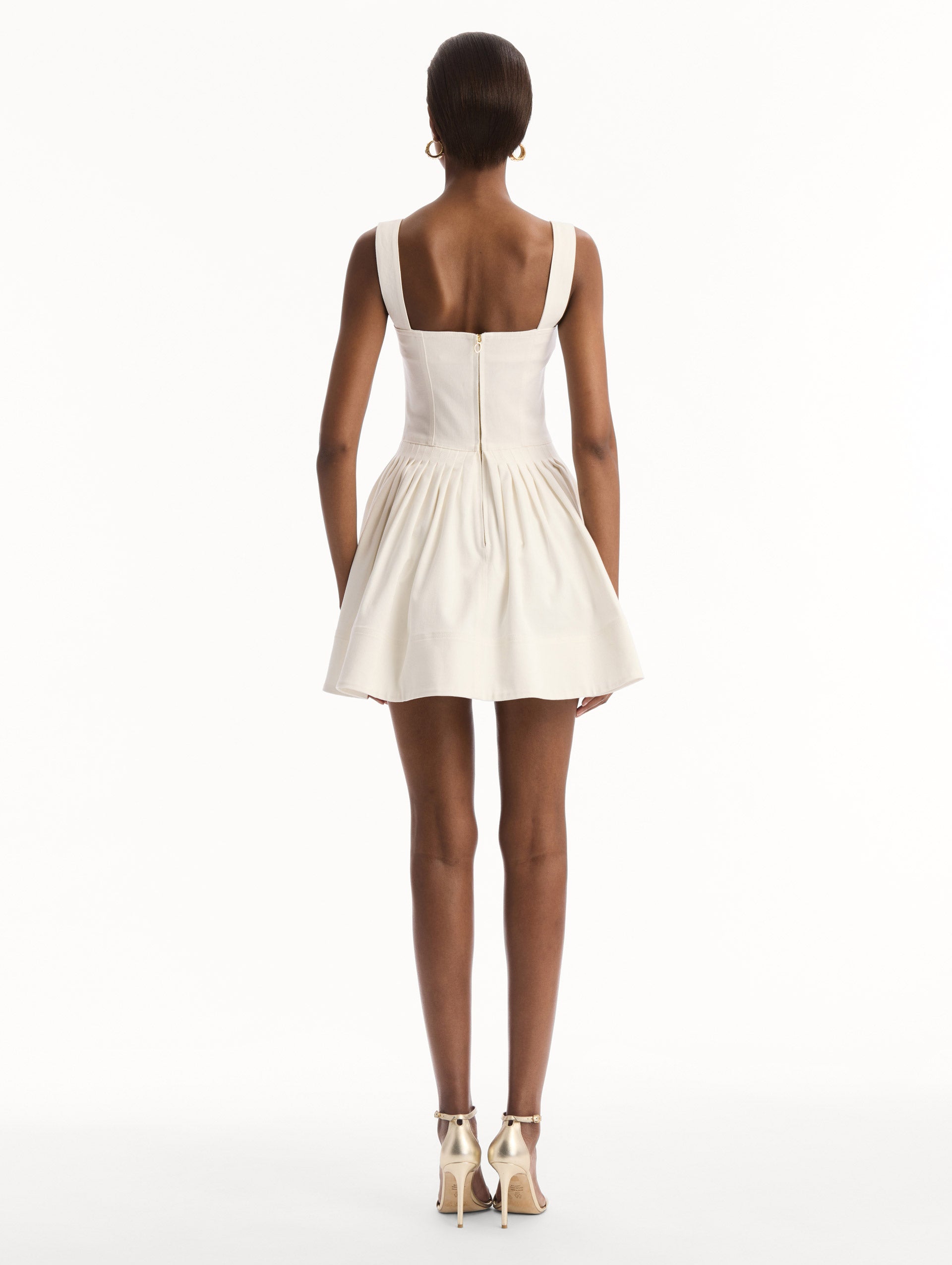 The model is wearing the pineapple appliqué denim dress with a structured bodice in the color white. Back view.