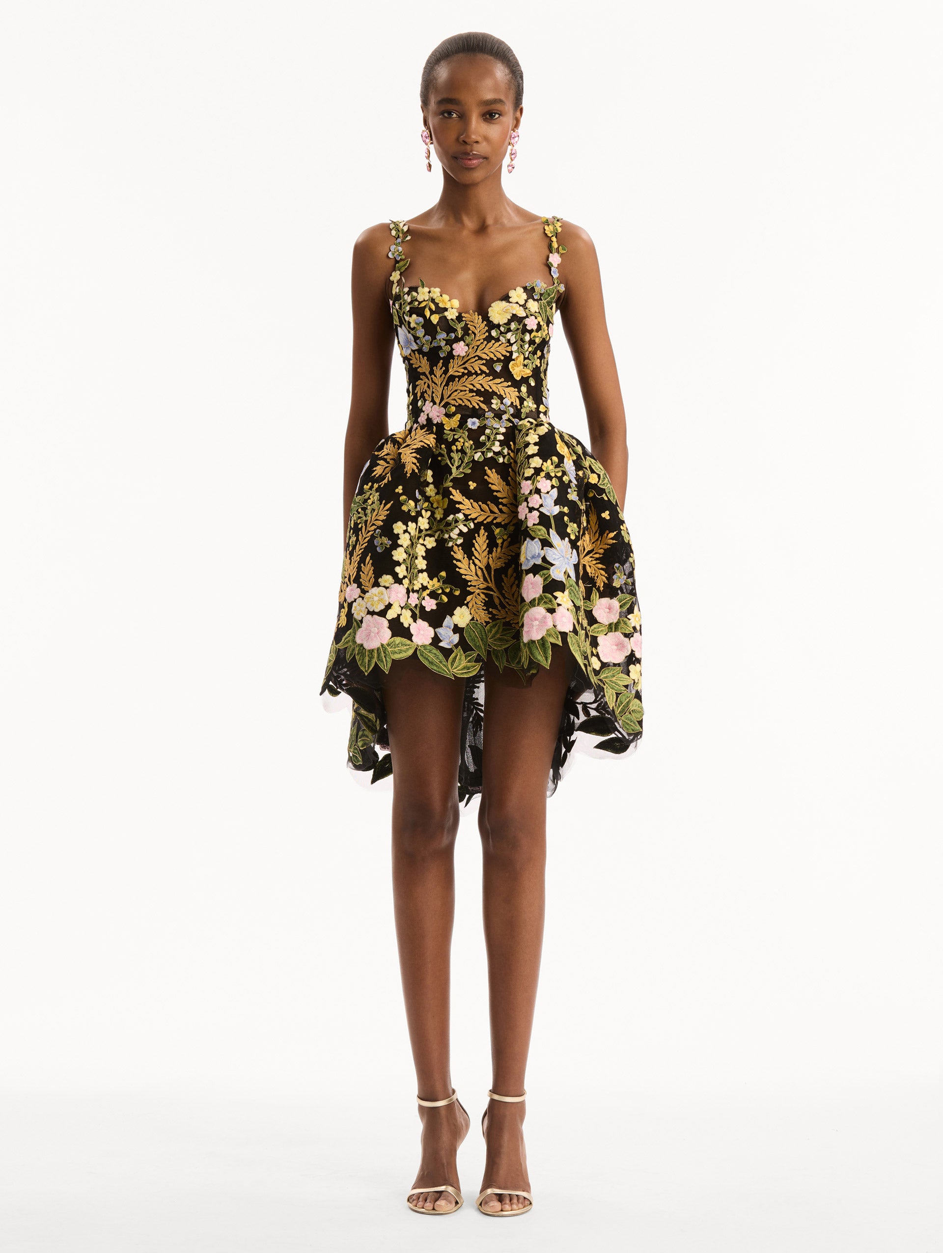 The model is wearing the Dominican Mixed-Floral Guipure High-Low Dress. Featuring a sweetheart neckline, delicate floral straps, fitted bodice, and mini skirt. Front View.