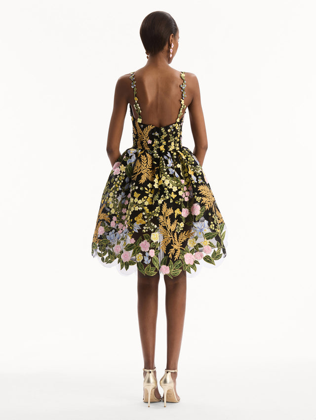The model is wearing the Dominican Mixed-Floral Guipure High-Low Dress. Featuring a sweetheart neckline, delicate floral straps, fitted bodice, and mini skirt. Back View.