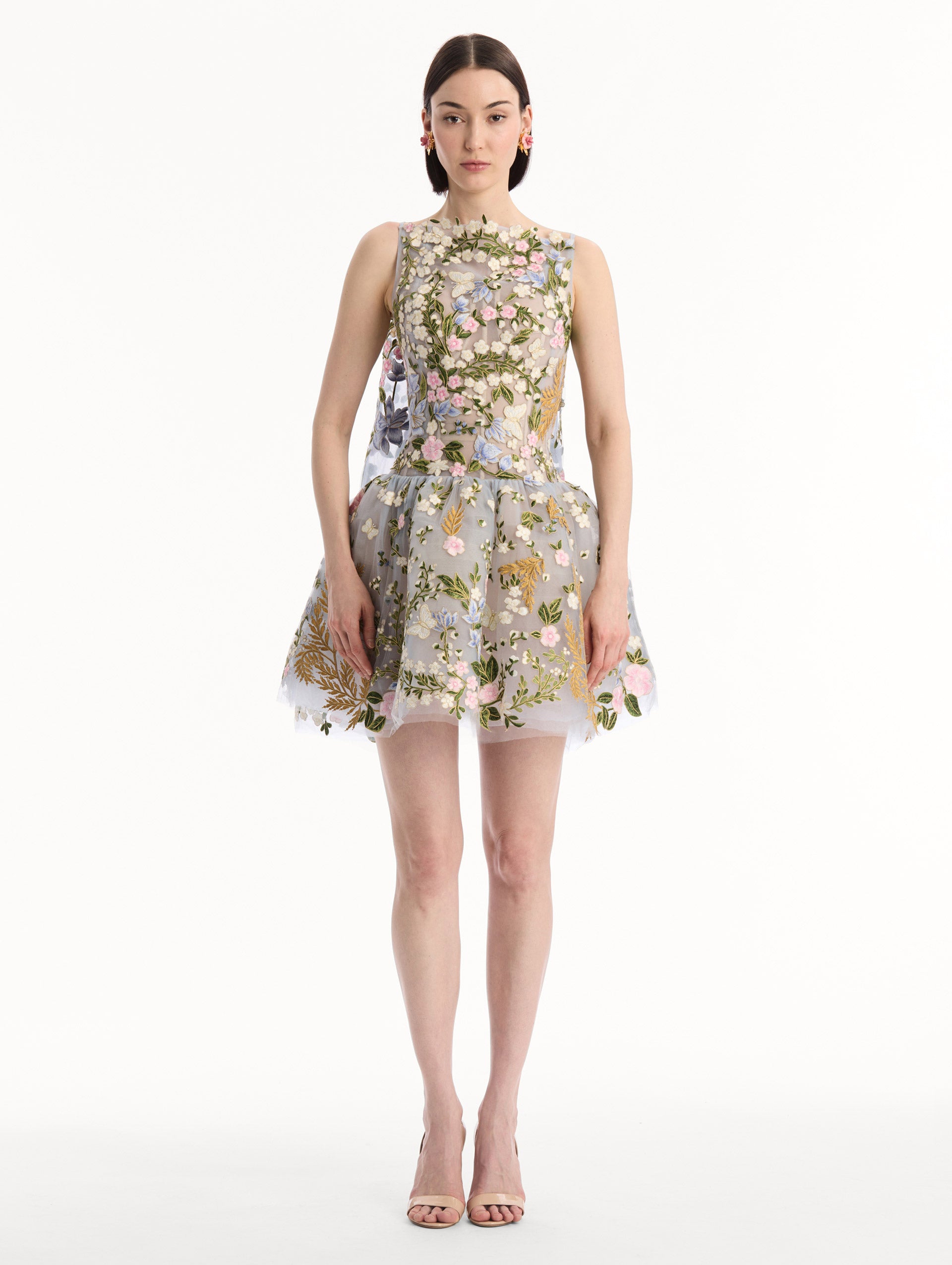 The model is wearing the Dominican Mixed-Floral Guipure Cape-Back Dress. Featuring a straight neckline, fitted bodice, flared mini skirt, and structural cape. Front View.