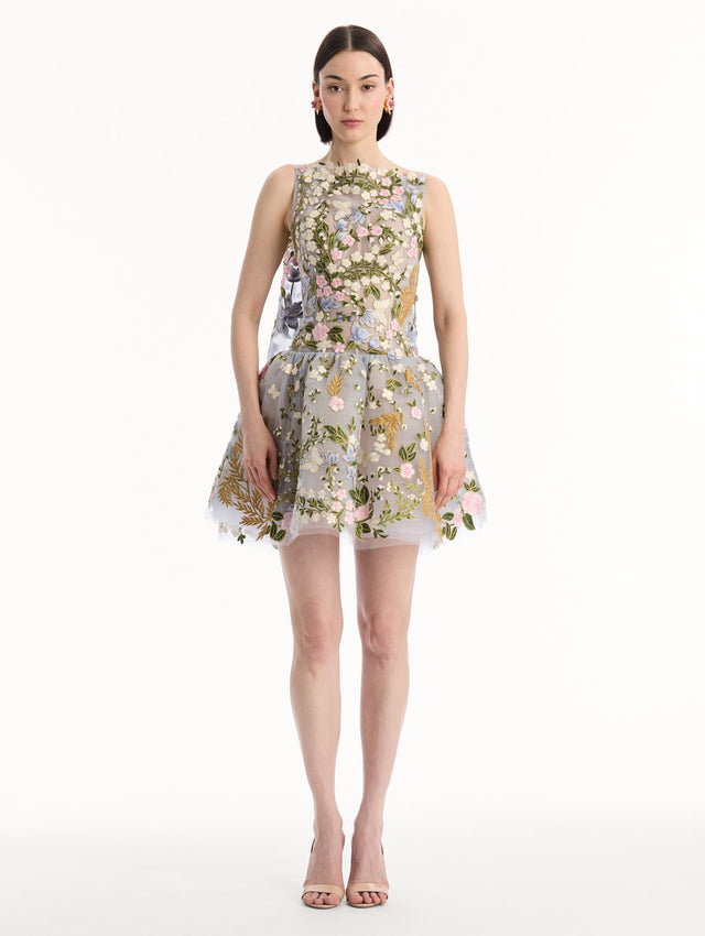 The model is wearing the Dominican Mixed-Floral Guipure Cape-Back Dress. Featuring a straight neckline, fitted bodice, flared mini skirt, and structural cape. Front View.