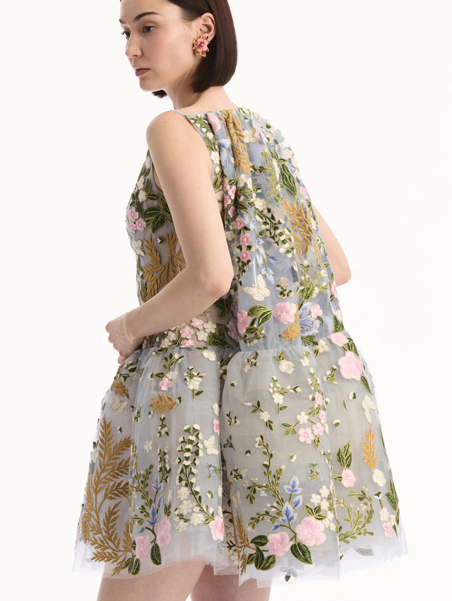 The model is wearing the Dominican Mixed-Floral Guipure Cape-Back Dress. Featuring a straight neckline, fitted bodice, flared mini skirt, and structural cape. Detail View.