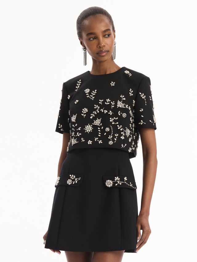 The model is wearing the Crystal Floral Embroidered Cocktail Dress in Black. Featuring faux front flap pockets with crystal embroidery and a structured mini skirt. Detail View.