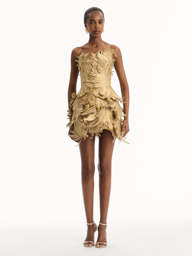 The model is wearing the Palm Leaves Metallic Cocktail Dress in Gold. Featuring dynamic palm leaves sculpted in metallic embroidery and a mini-length skirt. Front View.