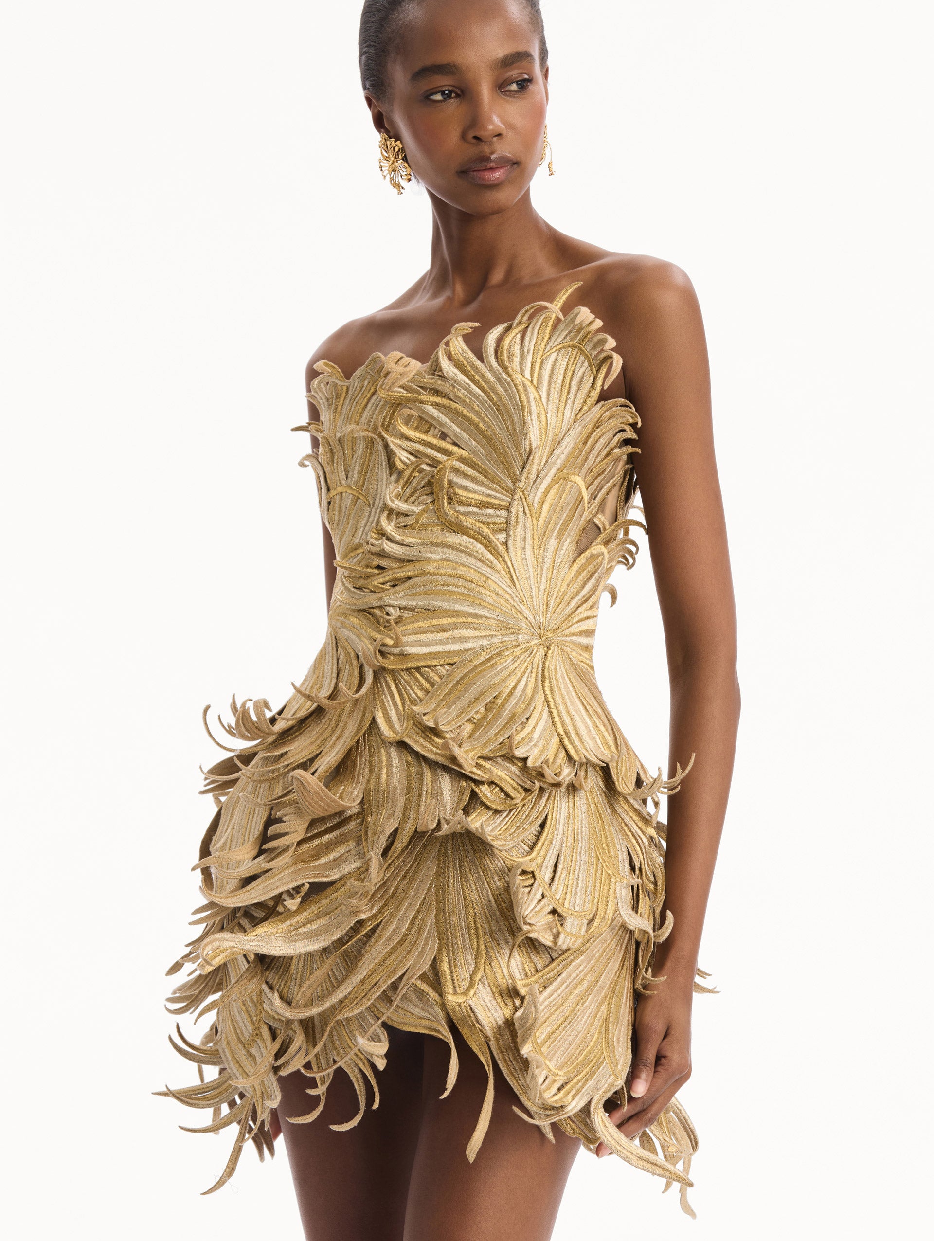 The model is wearing the Palm Leaves Metallic Cocktail Dress in Gold. Featuring dynamic palm leaves sculpted in metallic embroidery and a mini-length skirt. Detail View.