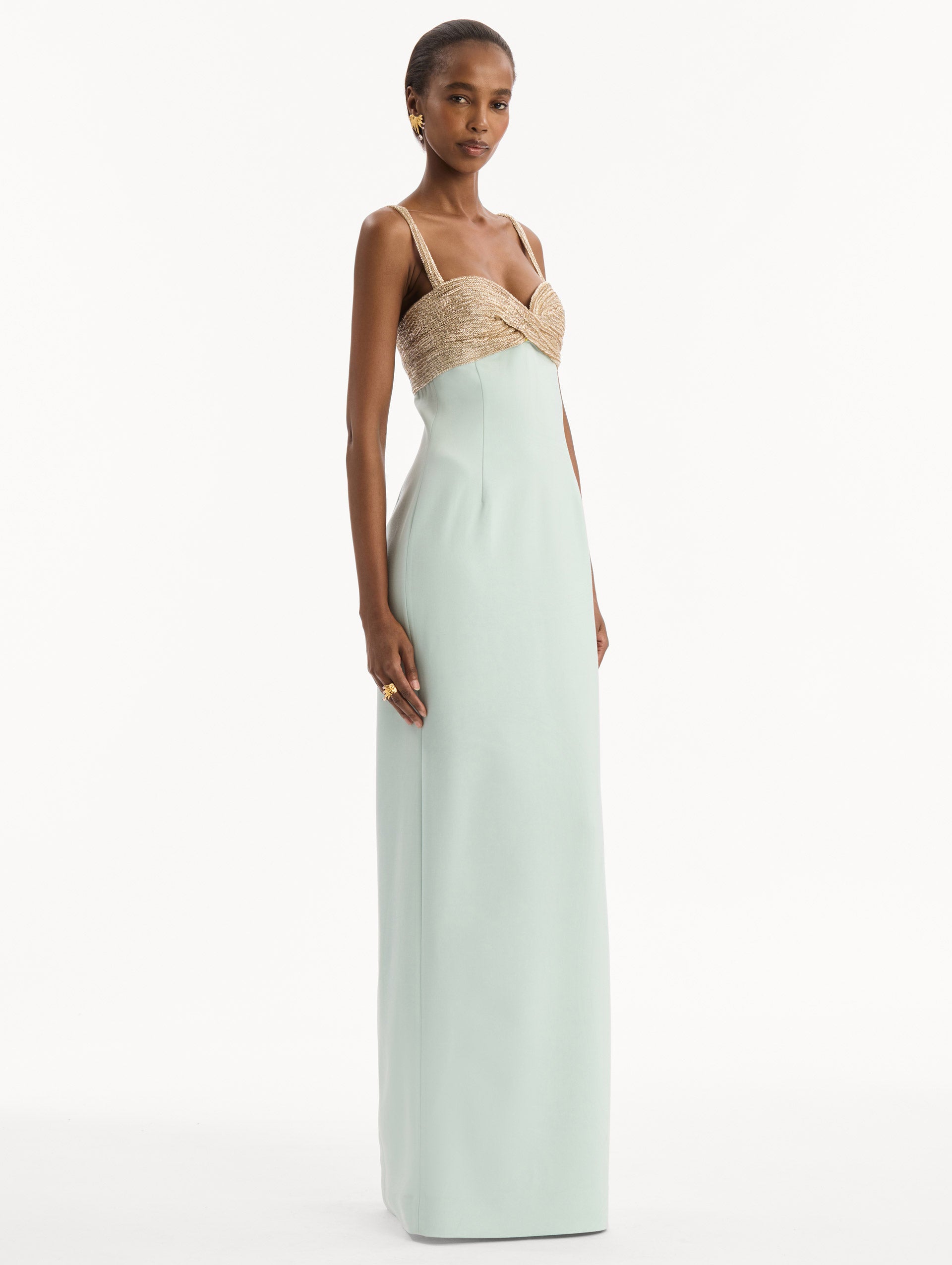 The model is wearing the Twist-Detail Metallic Column Gown in Saltwater Blue. Featuring a metallic twist-detail bodice and long, column silhouette. Side View.
