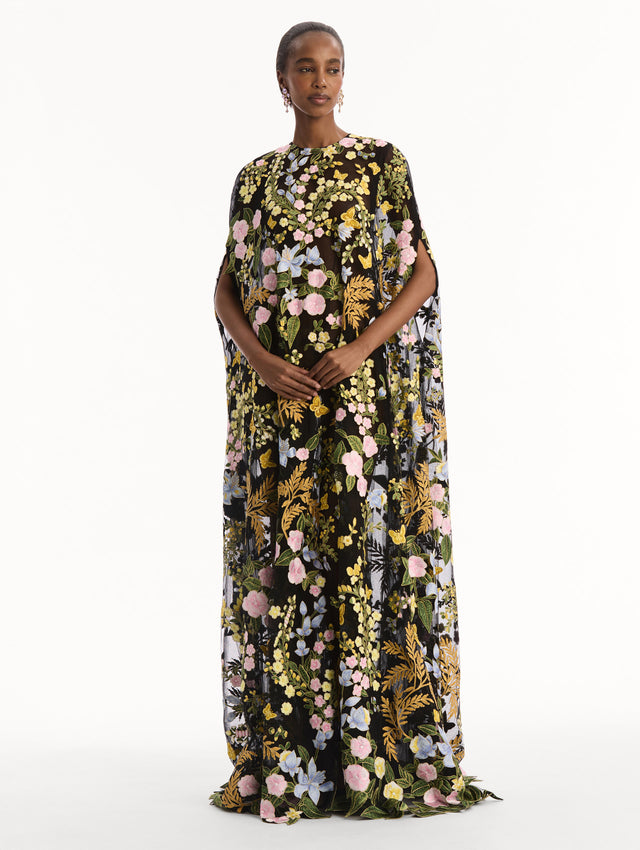 The model is wearing the Dominican Mixed-Floral Guipure Caftan. Featuring a long, flowing silhouette draping from the shoulders. Front View.