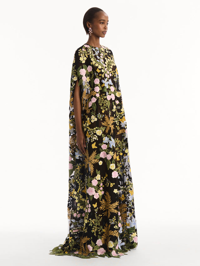 The model is wearing the Dominican Mixed-Floral Guipure Caftan. Featuring a long, flowing silhouette draping from the shoulders. Side View.