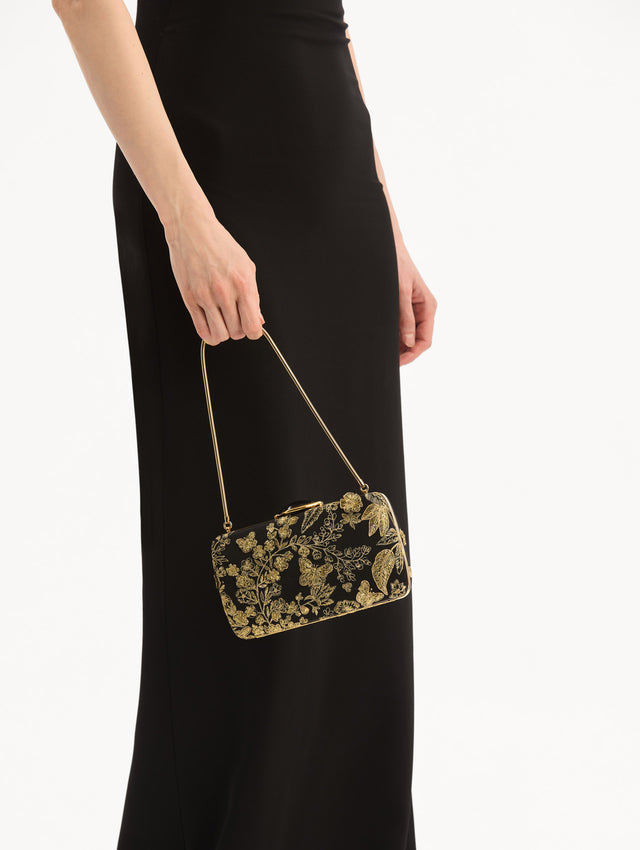 The model is wearing the Butterfly Embroidered O Minaudière in Black Satin with Gold Butterfly Embroidery. Detail View.