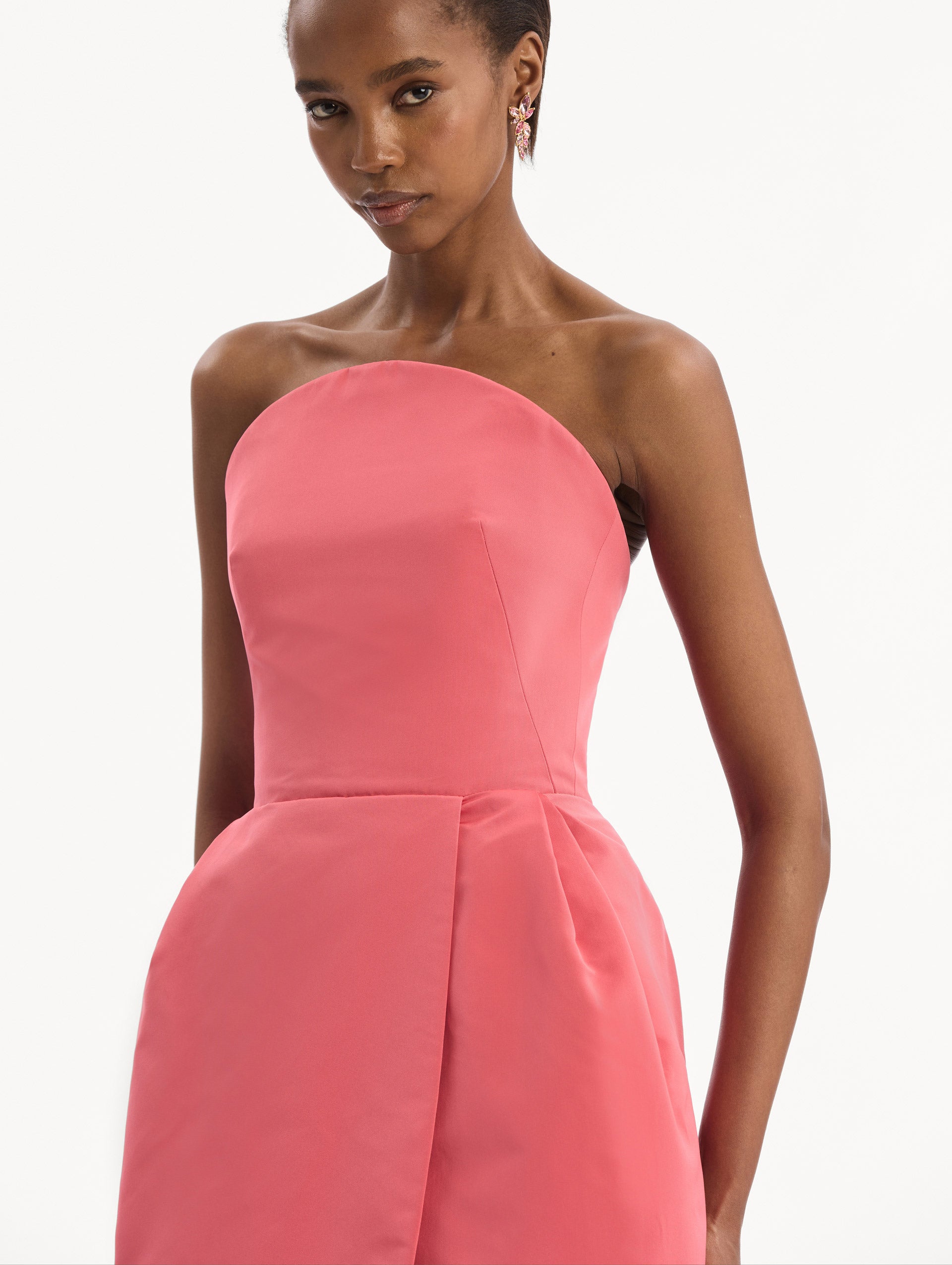 The model is wearing the Strapless Faille Gown in Guava Pink. Featuring a sculpted silhouette and wrap-style skirt with an asymmetrical hem. Detail View.