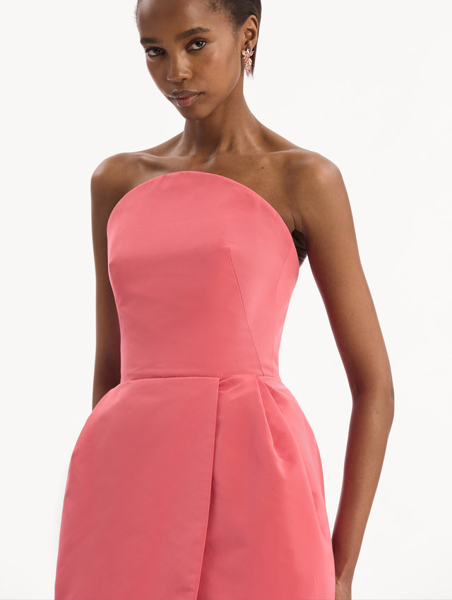 The model is wearing the Strapless Faille Gown in Guava Pink. Featuring a sculpted silhouette and wrap-style skirt with an asymmetrical hem. Detail View.