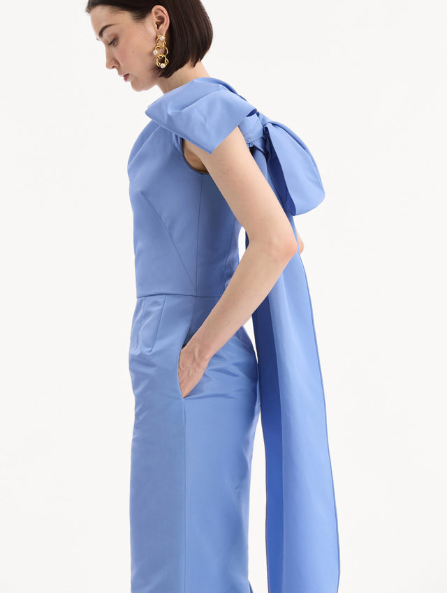 The model is wearing the Bow-Detail Faille Column Gown in a periwinkle blue. Featuring a column silhouette and sculptural bow detail at the shoulder. Detail View.