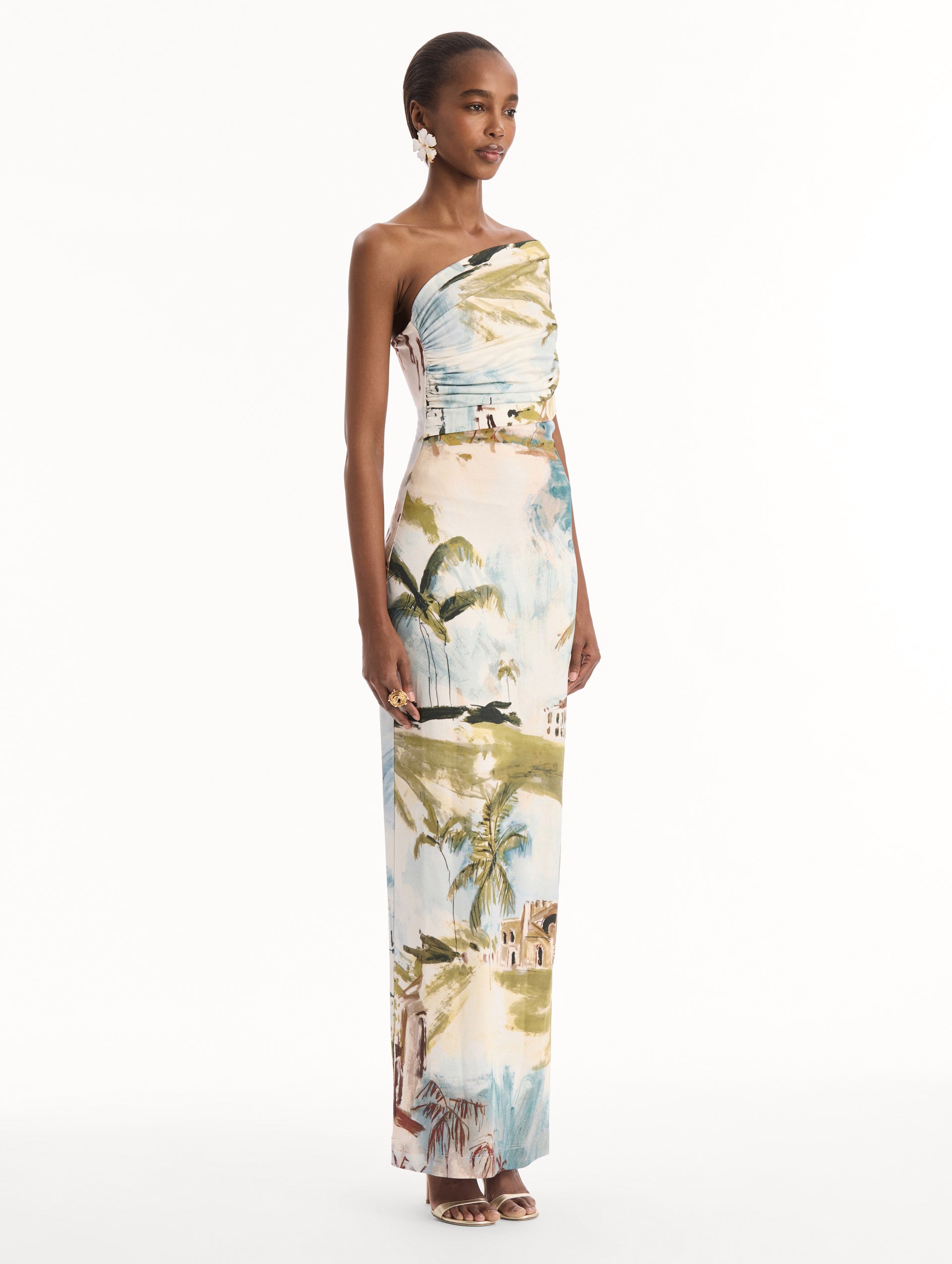 The model is wearing the Dominican Landscape Jersey Gown. Featuring a one-shoulder neckline and long, column silhouette. Side View.