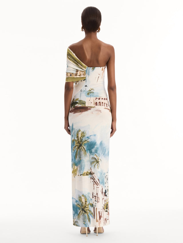 The model is wearing the Dominican Landscape Jersey Gown. Featuring a one-shoulder neckline and long, column silhouette. Back View.