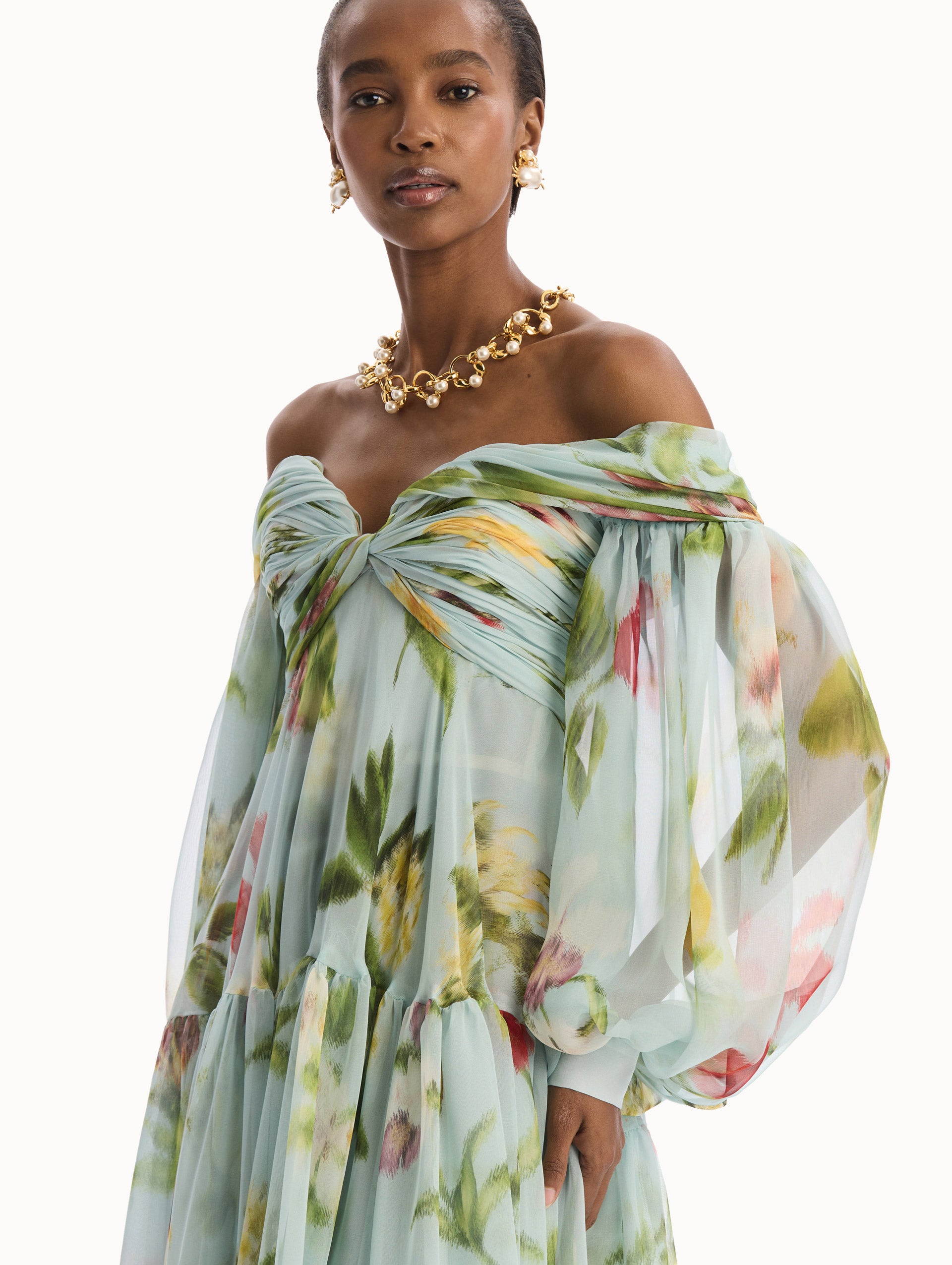 The model is wearing the Chiné Dominican Mixed-Floral Chiffon Sweetheart Gown. Featuring an off-the-shoulder sweetheart neckline, long sleeves, and flowing, tiered skirt. Detail View.