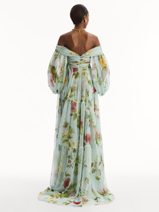 The model is wearing the Chiné Dominican Mixed-Floral Chiffon Sweetheart Gown. Featuring an off-the-shoulder sweetheart neckline, long sleeves, and flowing, tiered skirt. Back View.