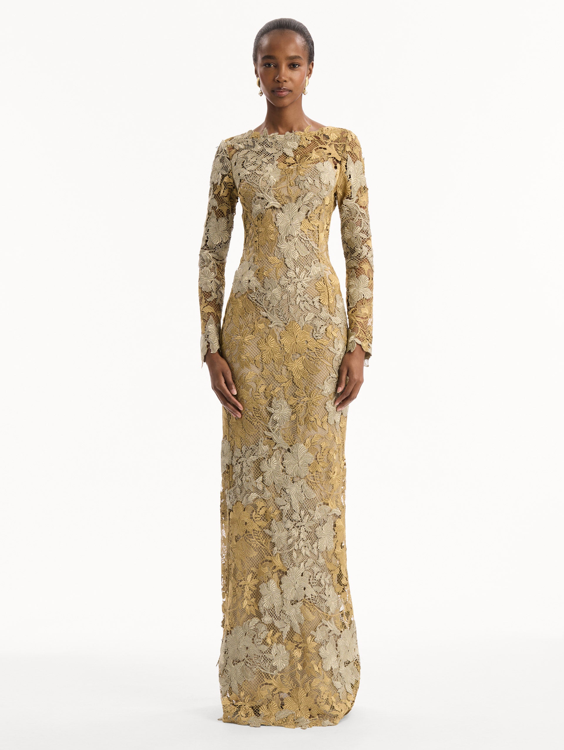 The model is wearing the Hibiscus Metallic Guipure Gown. Featuring metallic guipure lace, long sleeves, a fitted silhouette, and long skirt. Front View.