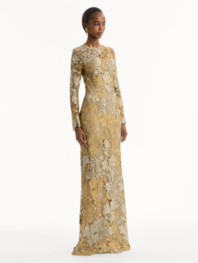 The model is wearing the Hibiscus Metallic Guipure Gown. Featuring metallic guipure lace, long sleeves, a fitted silhouette, and long skirt. Side View.