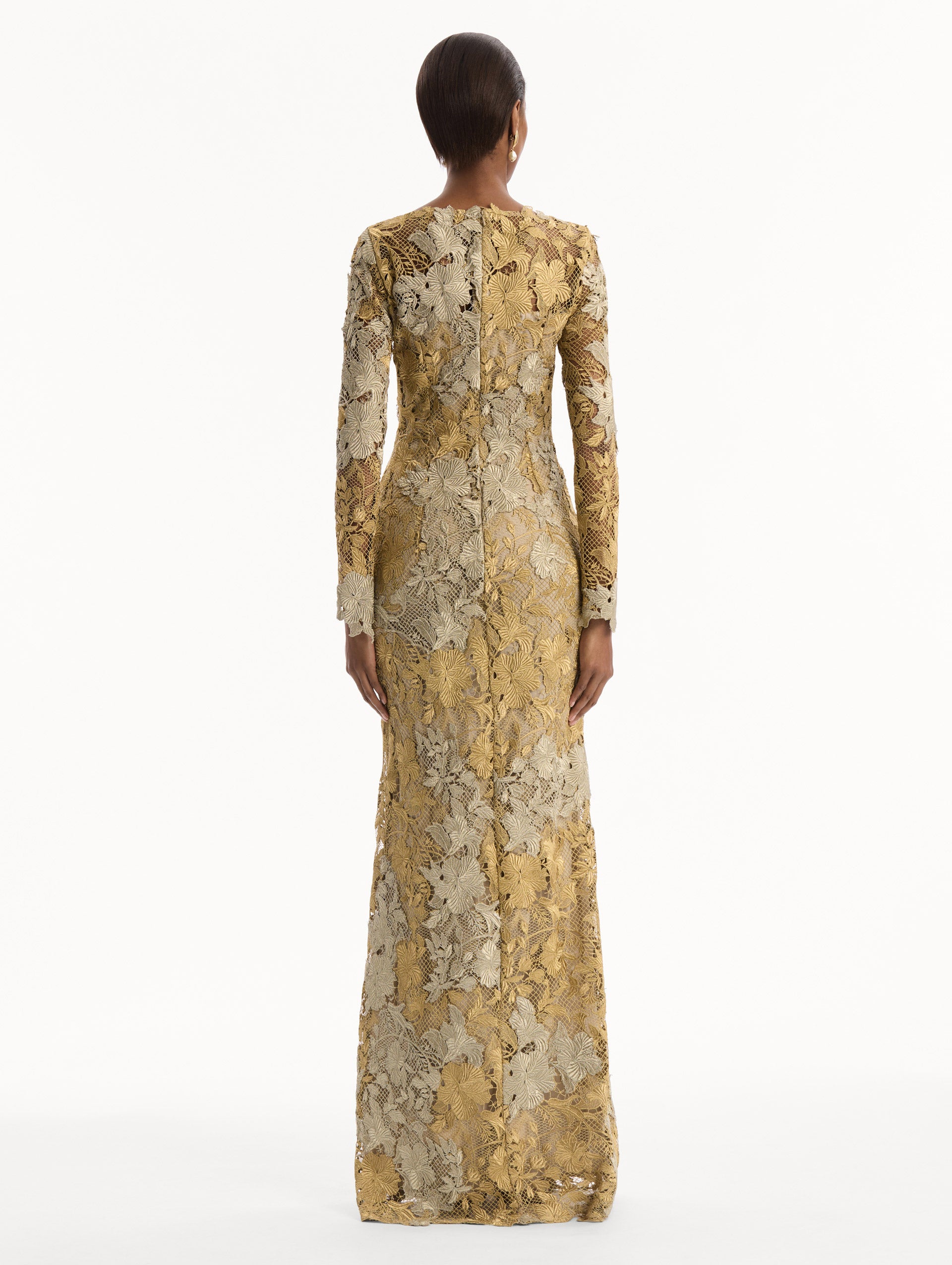 The model is wearing the Hibiscus Metallic Guipure Gown. Featuring metallic guipure lace, long sleeves, a fitted silhouette, and long skirt. Back View.