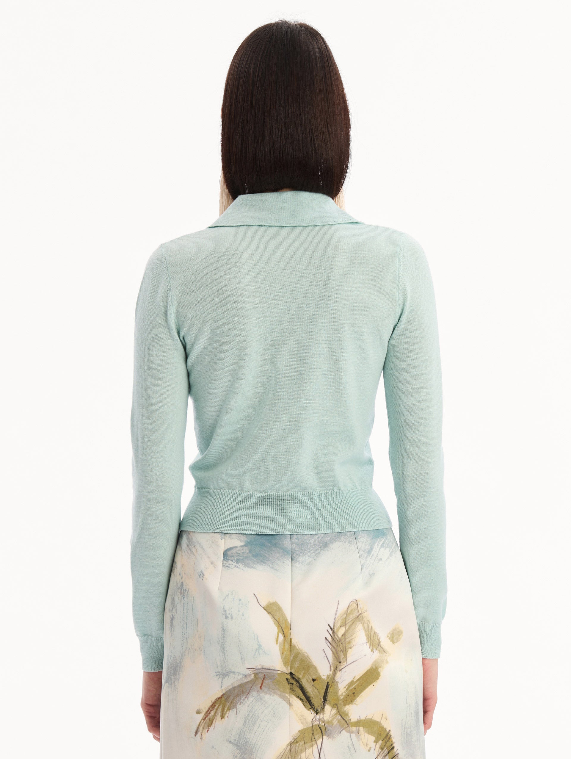 The model is wearing the Wool Polo Pullover in Saltwater Blue. Featuring an open color neckline, long sleeves, and ribbed trim. Back View.