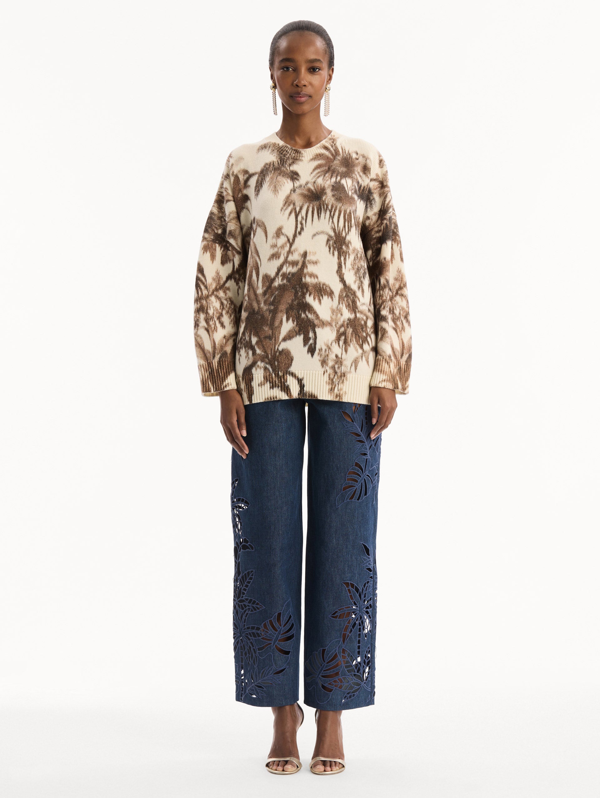 The model is wearing the Chiné Palm Leaves Oversized Pullover in ivory printed with brown palm leaves. Featuring a relaxed silhouette, crew neckline, and ribbed trims. Front View.