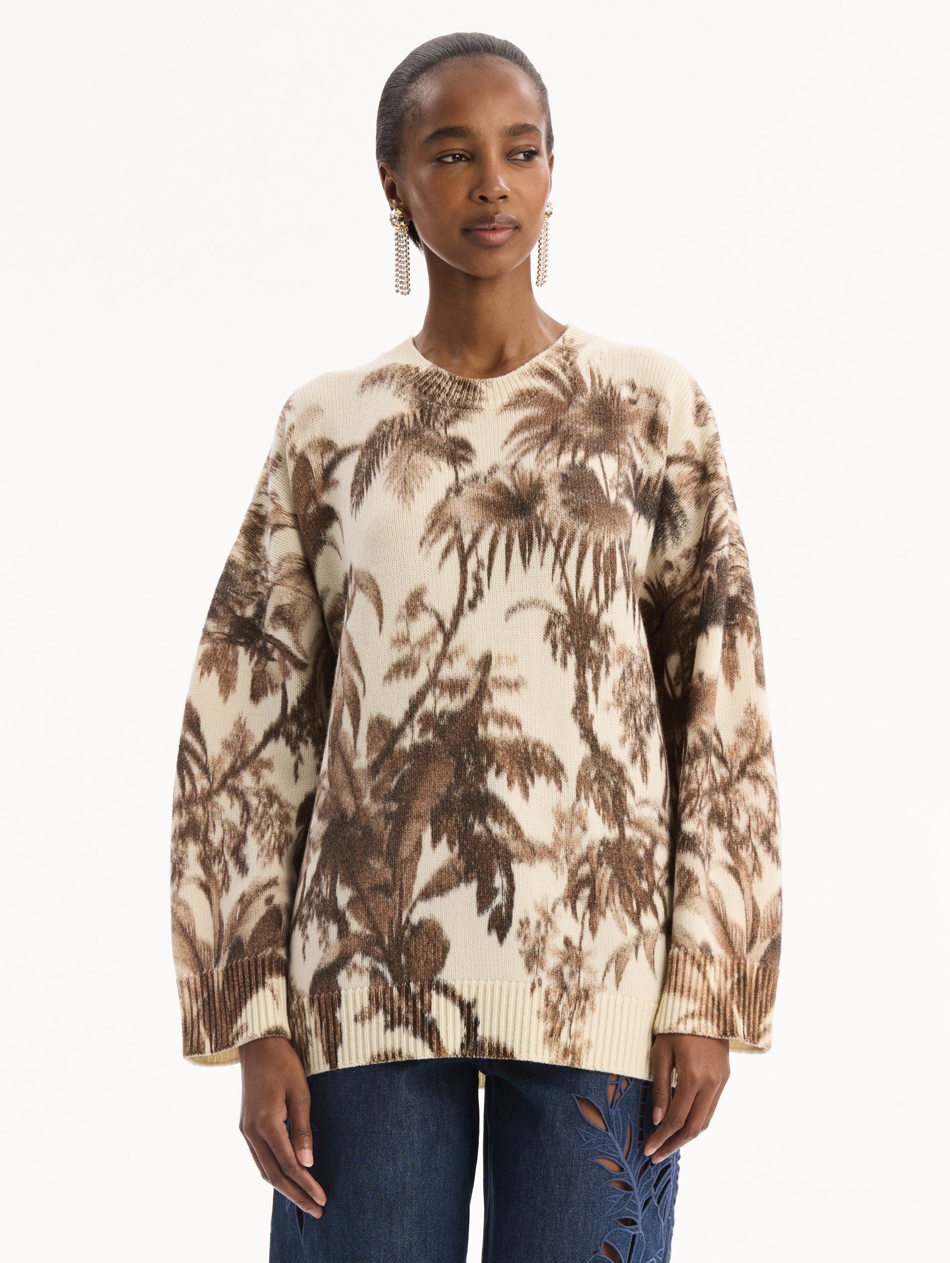 The model is wearing the Chiné Palm Leaves Oversized Pullover in ivory printed with brown palm leaves. Featuring a relaxed silhouette, crew neckline, and ribbed trims. Front View.
