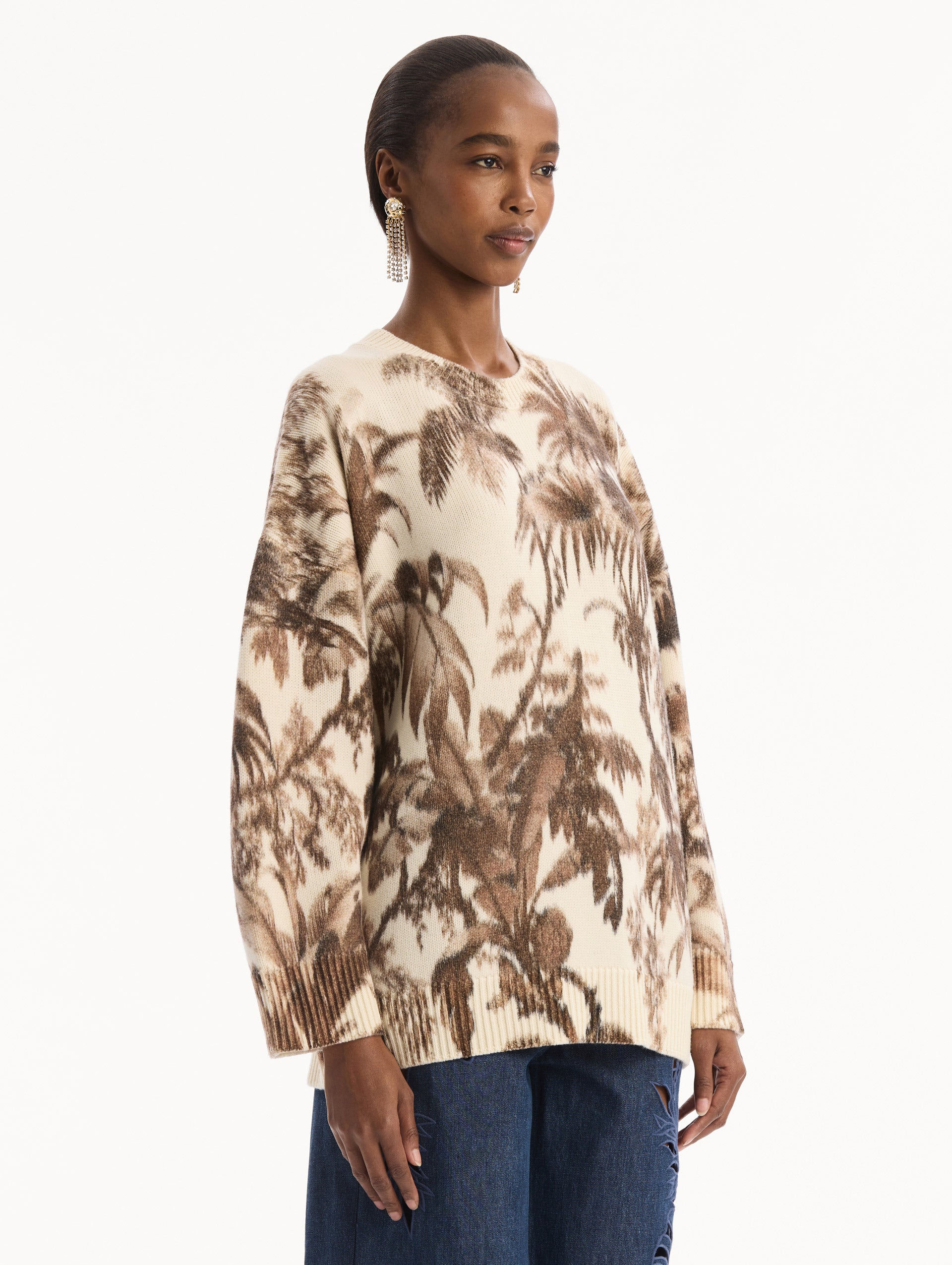 The model is wearing the Chiné Palm Leaves Oversized Pullover in ivory printed with brown palm leaves. Featuring a relaxed silhouette, crew neckline, and ribbed trims. Side View.