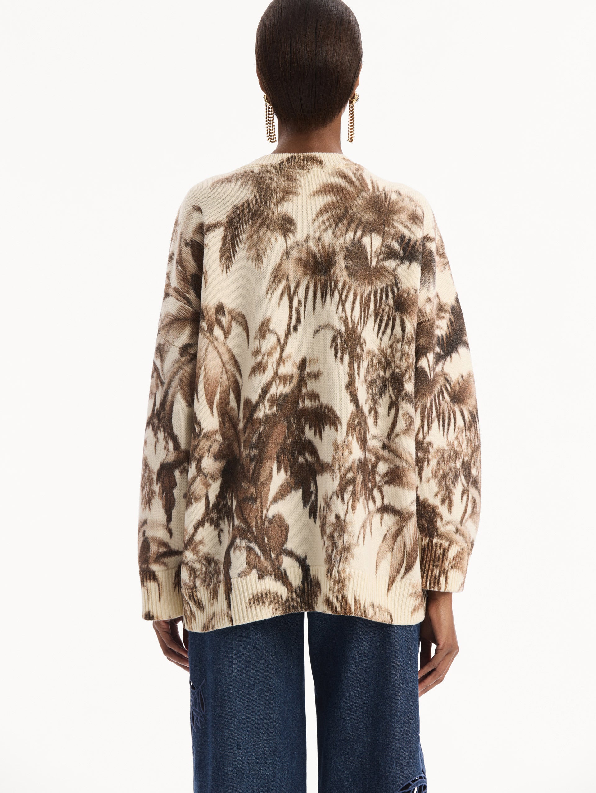 The model is wearing the Chiné Palm Leaves Oversized Pullover in ivory printed with brown palm leaves. Featuring a relaxed silhouette, crew neckline, and ribbed trims. Back View.