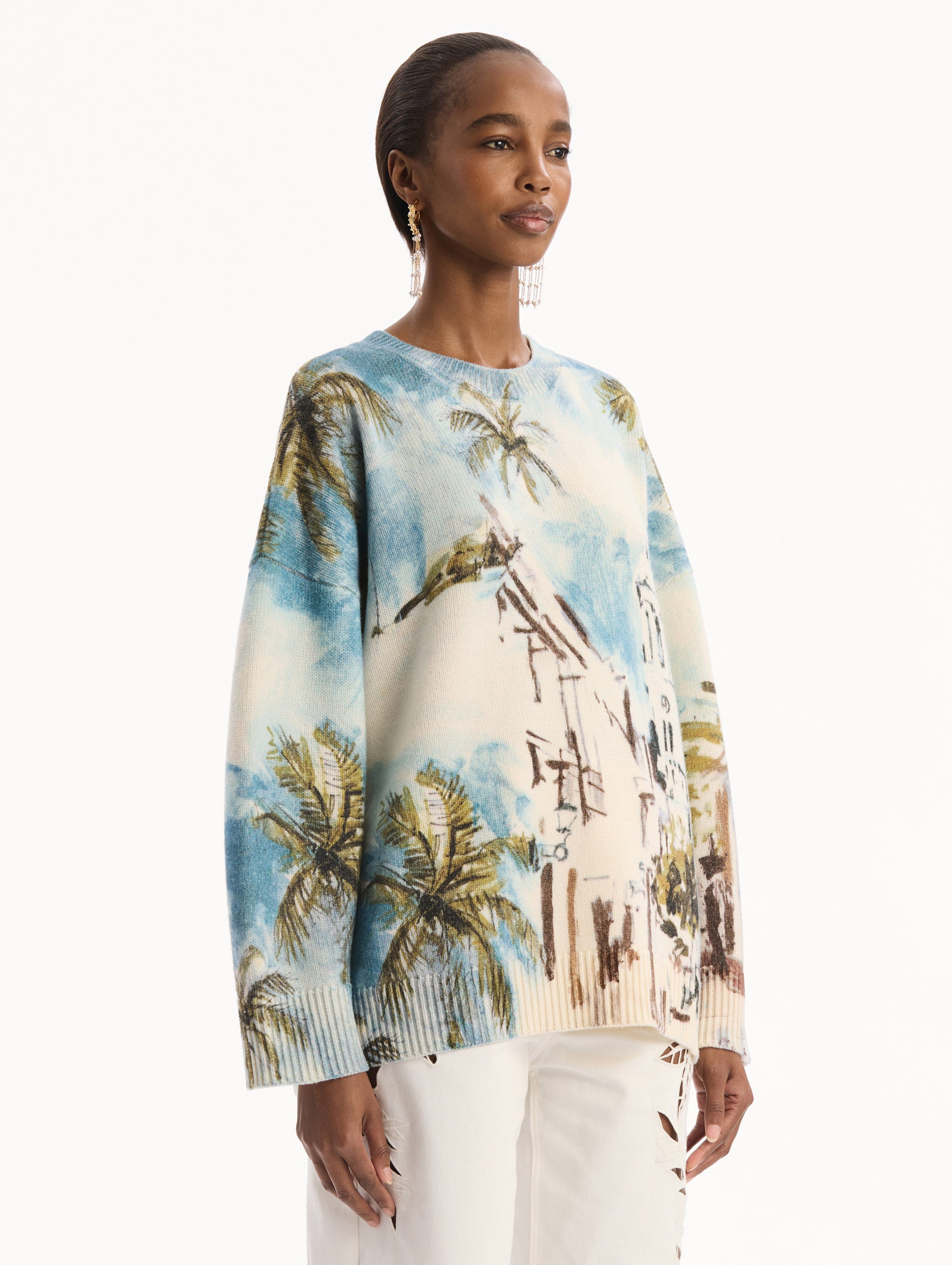 The model is wearing the Dominican Landscape Oversized Pullover. Featuring a crew neckline, long sleeves, ribbed trim, and an oversized fit. Side View.