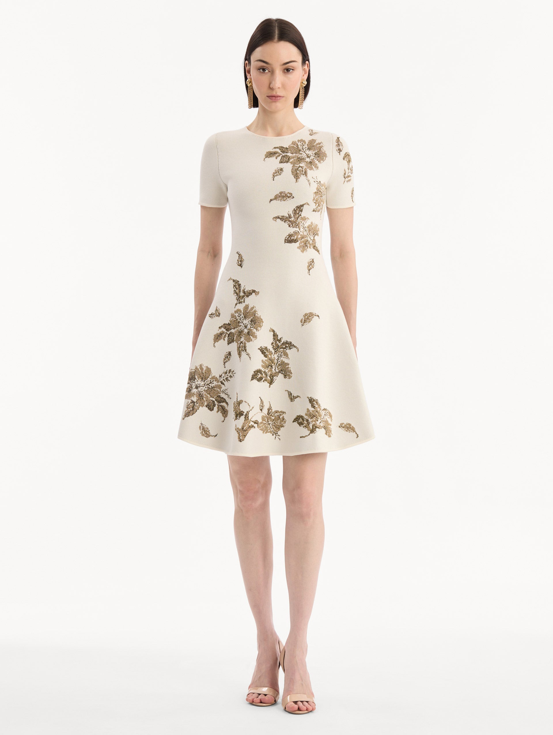 The model is wearing the Hibiscus Metallic Jacquard Dress in Ivory with Gold hibiscus motifs. Featuring short sleeves, a softly structured silhouette, and mini-length skirt. Front View.
