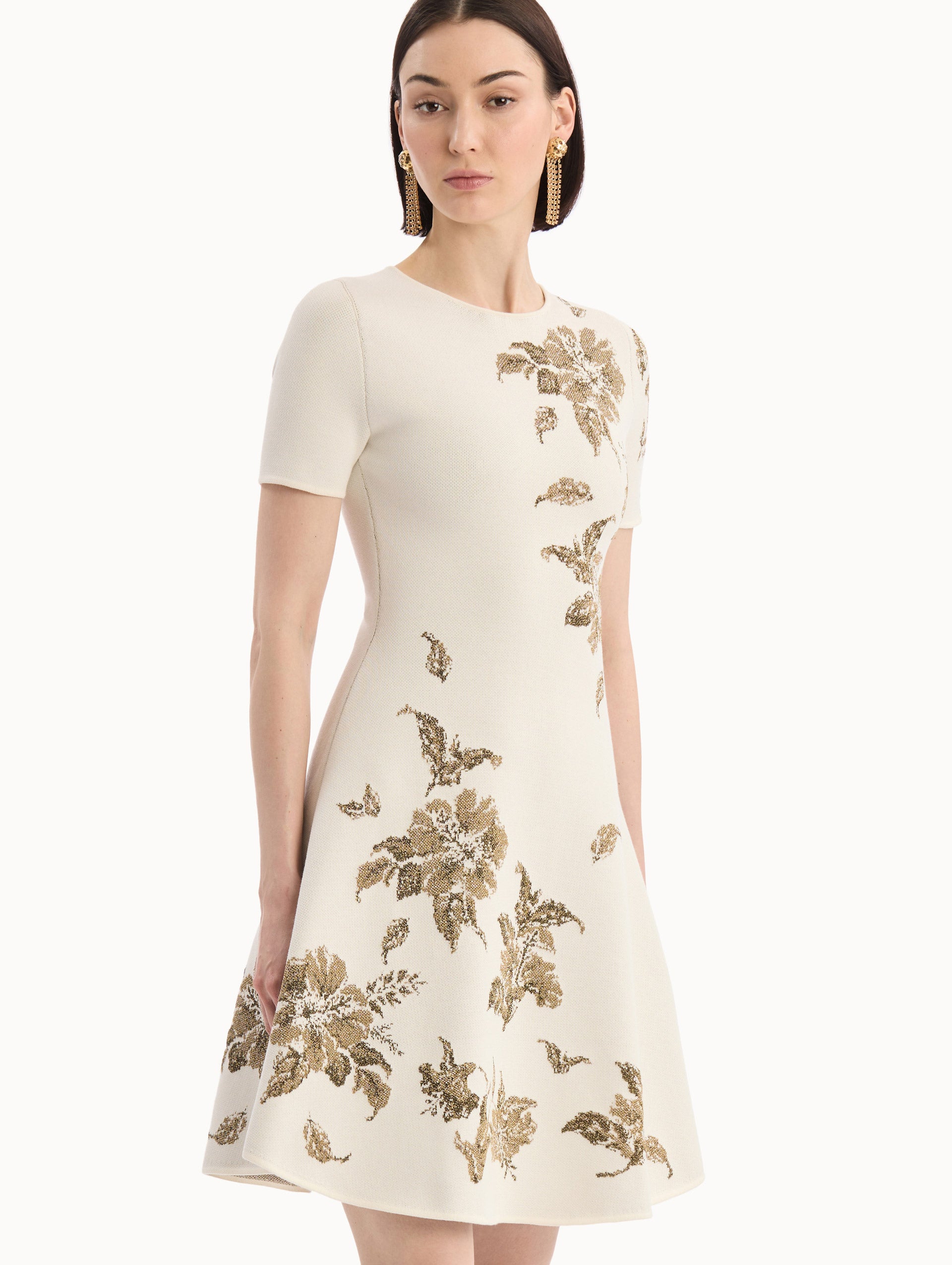The model is wearing the Hibiscus Metallic Jacquard Dress in Ivory with Gold hibiscus motifs. Featuring short sleeves, a softly structured silhouette, and mini-length skirt. Detail View.