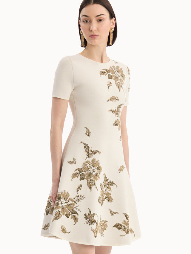 The model is wearing the Hibiscus Metallic Jacquard Dress in Ivory with Gold hibiscus motifs. Featuring short sleeves, a softly structured silhouette, and mini-length skirt. Detail View.