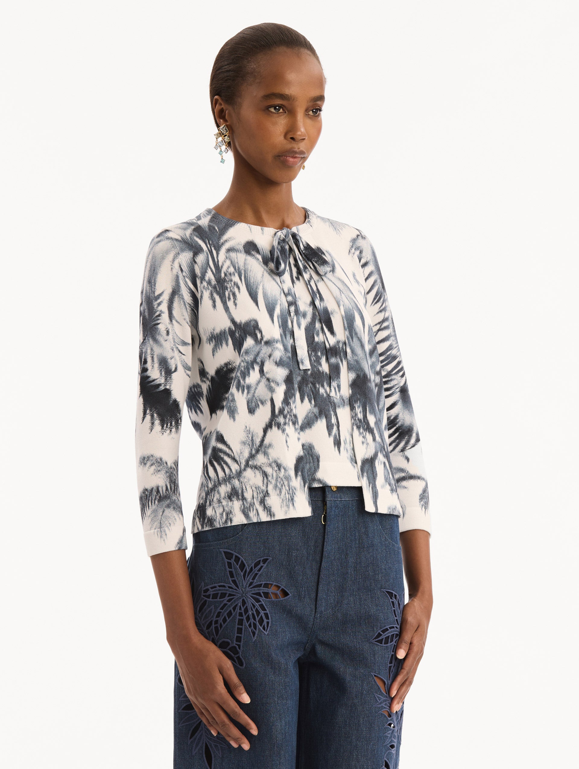 The model is wearing the Chiné Palm Leaves Cardigan in Navy and White. Featuring a crew neckline, quarter-length sleeves, banded trim, and tie front closure. Side View.