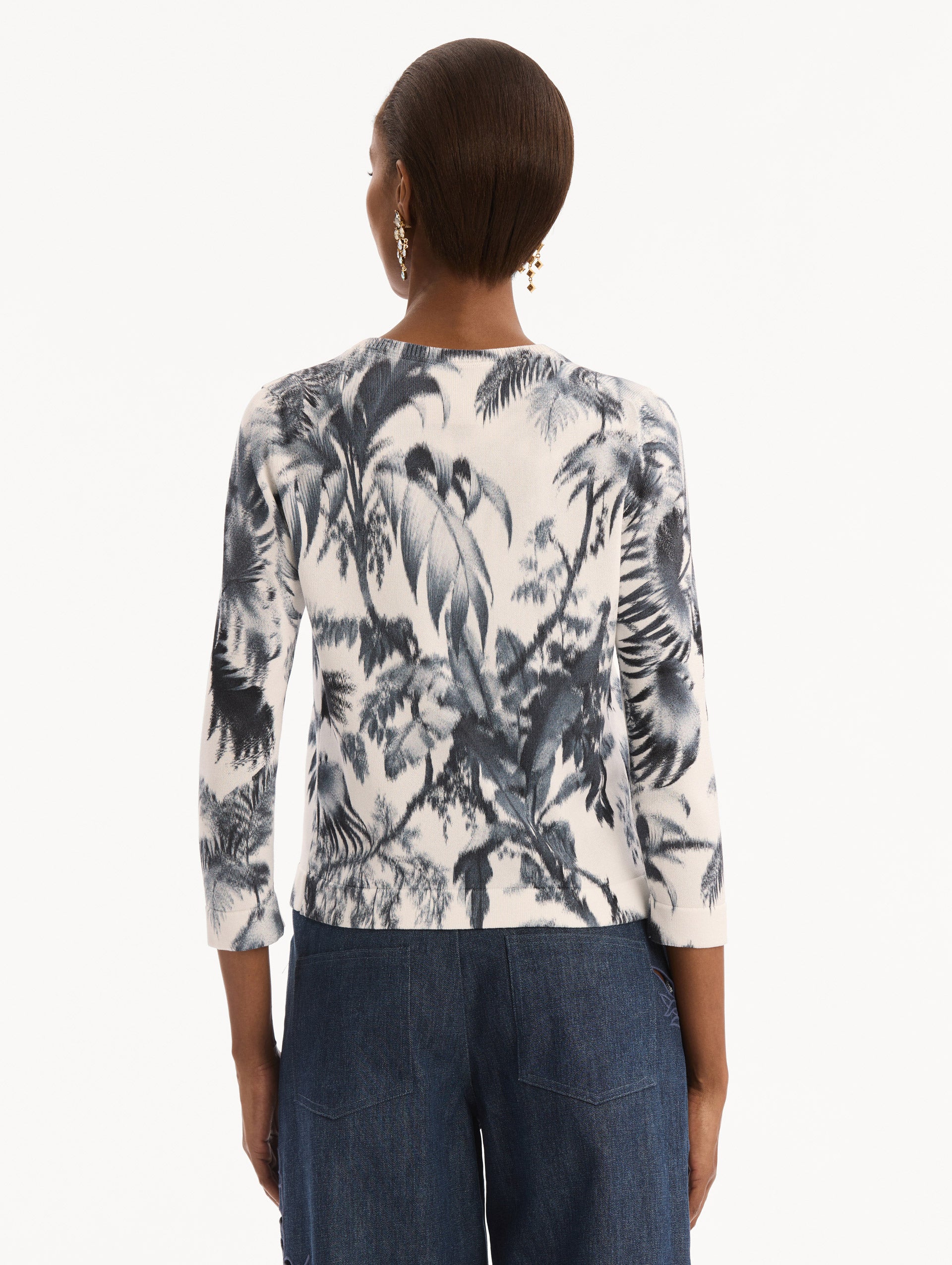 The model is wearing the Chiné Palm Leaves Cardigan in Navy and White. Featuring a crew neckline, quarter-length sleeves, banded trim, and tie front closure. Back View.