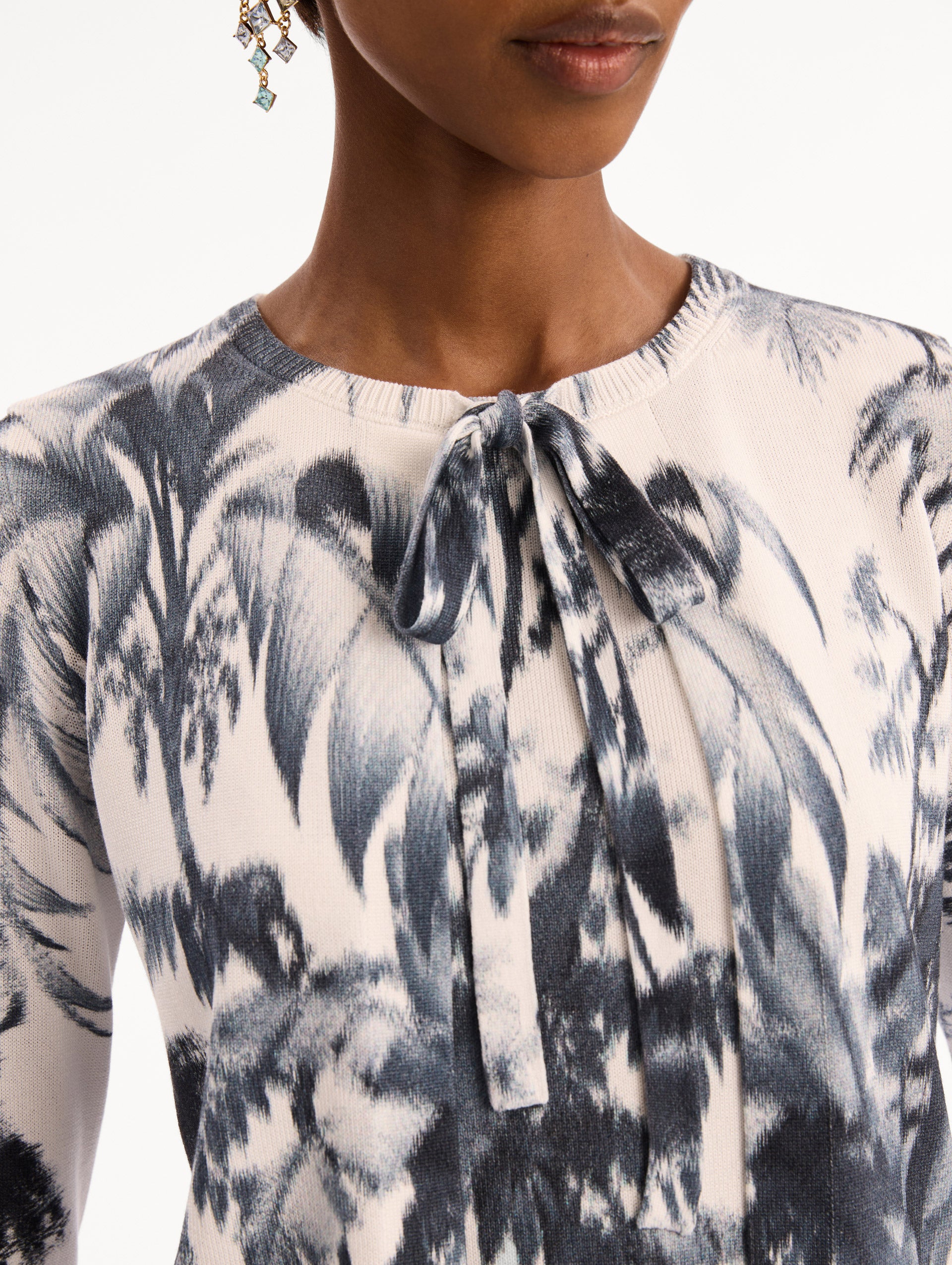The model is wearing the Chiné Palm Leaves Cardigan in Navy and White. Featuring a crew neckline, quarter-length sleeves, banded trim, and tie front closure. Detail View.