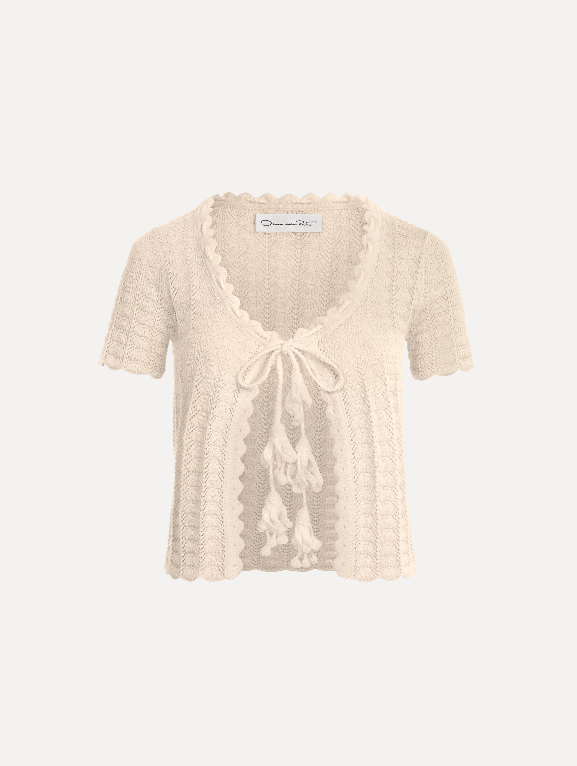 The Pointelle Weave Cardigan in Ivory. Featuring a scoop neckline, short sleeves, scalloped edges, and a front tie closure. Front View.