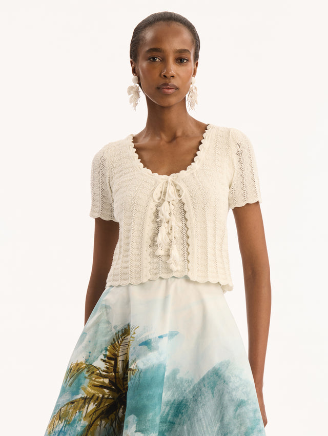 Ivory Pointelle Weave Cardigan. Shortsleeved, Scalloped edges. Bow and Tassel Closure. Front View.