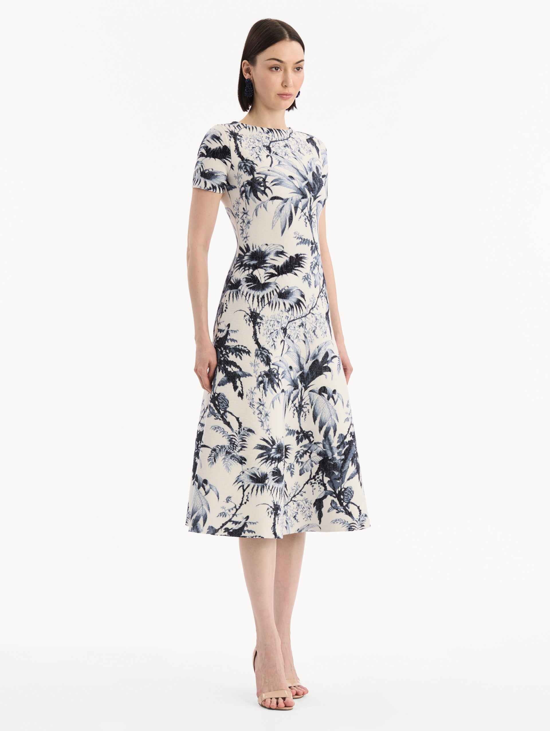 The model is wearing the Chiné Palm Leaves Knit Dress in Navy and Ivory. Featuring a classic silhouette with short sleeves and an A-line midi skirt. Side View.