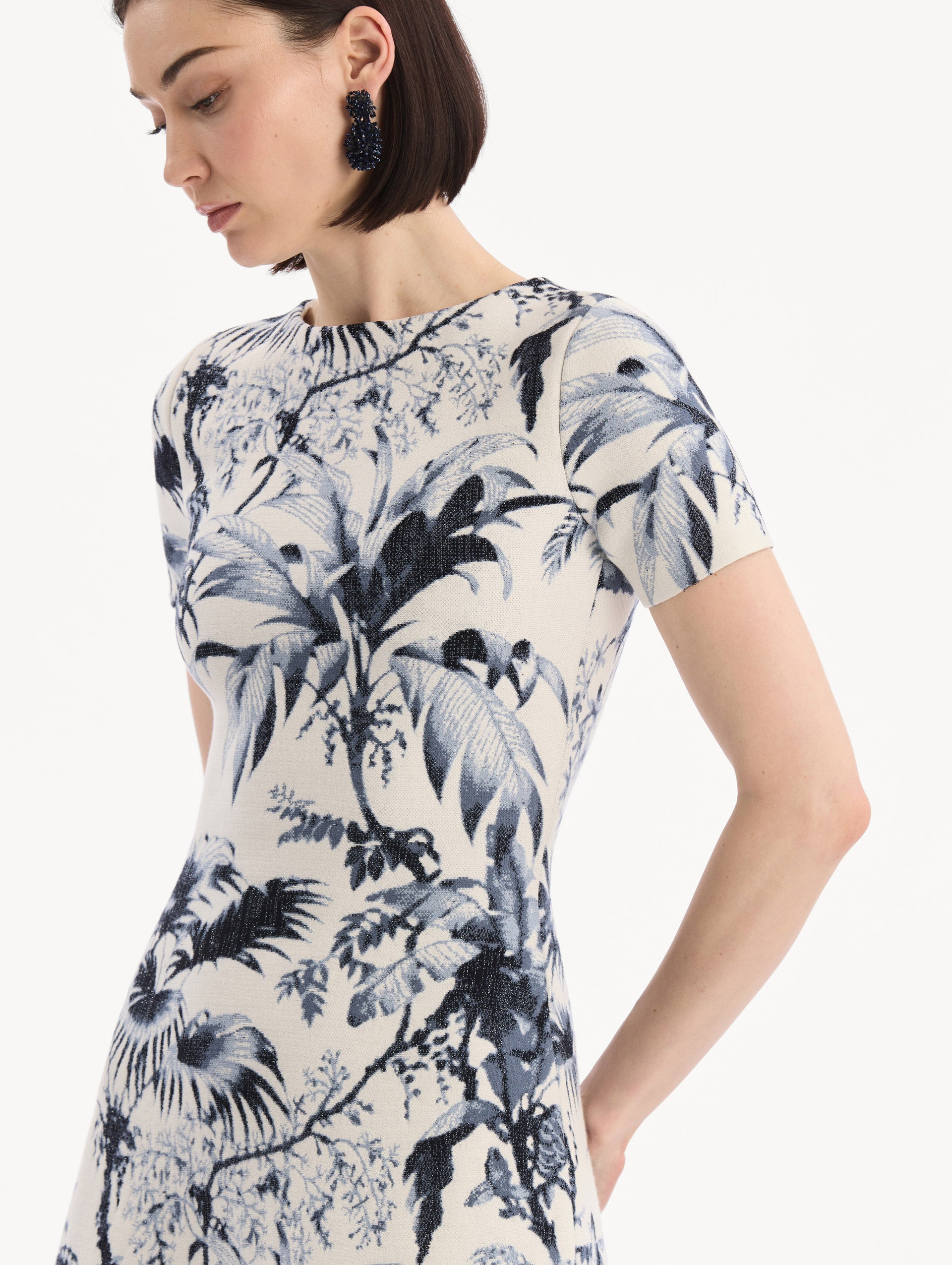 The model is wearing the Chiné Palm Leaves Knit Dress in Navy and Ivory. Featuring a classic silhouette with short sleeves and an A-line midi skirt. Detail View.