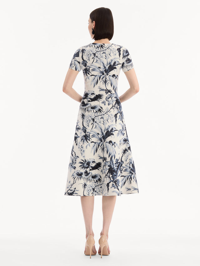 The model is wearing the Chiné Palm Leaves Knit Dress in Navy and Ivory. Featuring a classic silhouette with short sleeves and an A-line midi skirt. Back View.