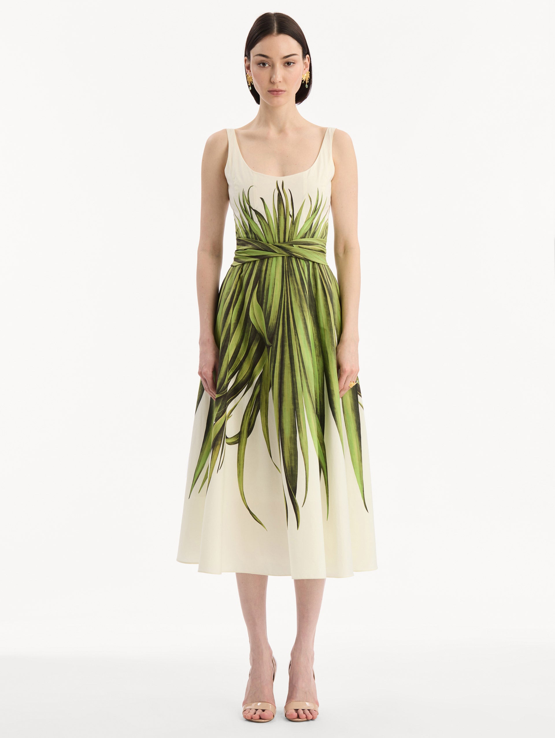 The model is wearing the Palm Leaves Cotton Poplin Dress. Featuring a scoop neckline, tank straps, cinched waist, and midi length. Front View.