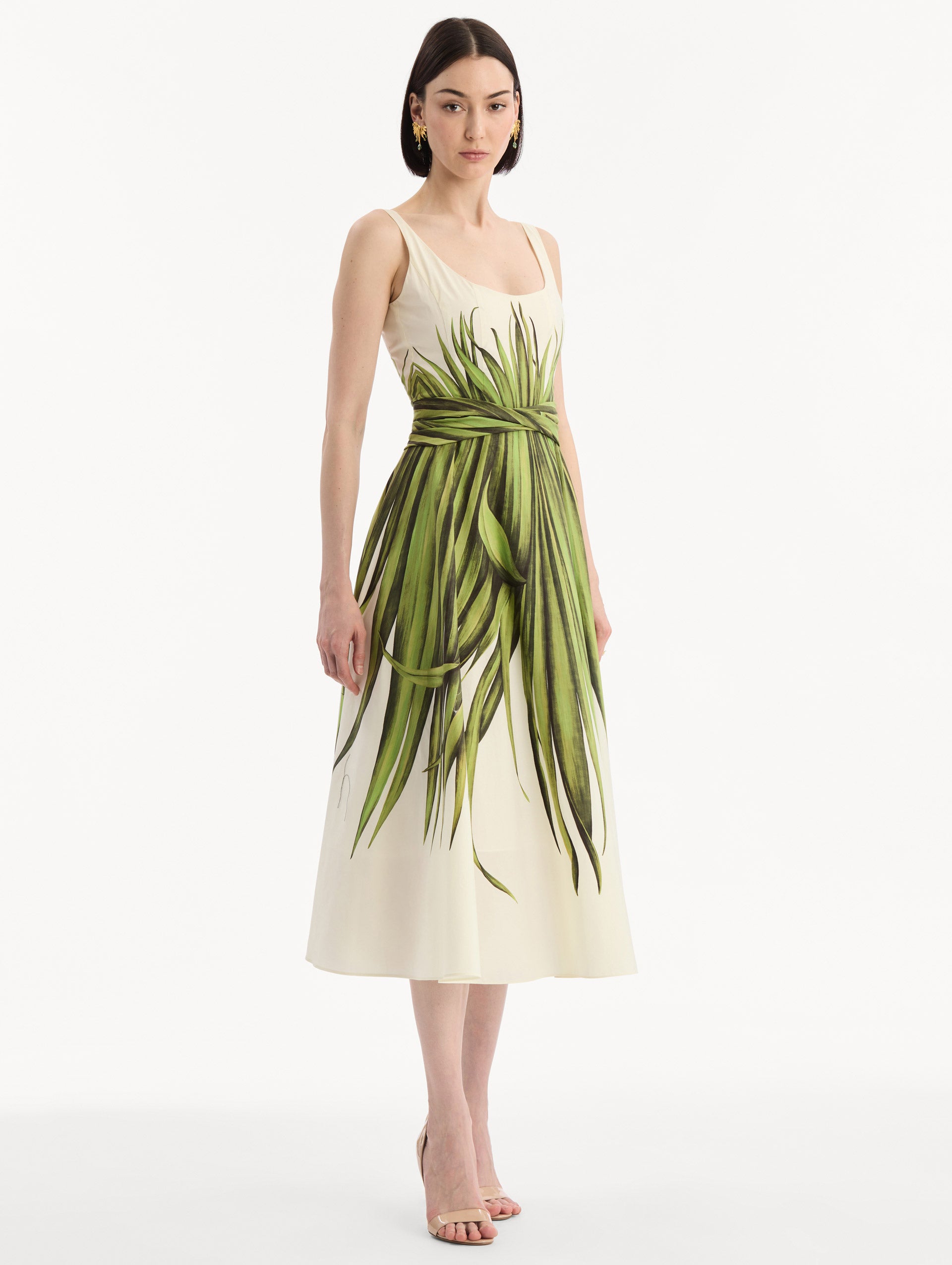 The model is wearing the Palm Leaves Cotton Poplin Dress. Featuring a scoop neckline, tank straps, cinched waist, and midi length. Side View.
