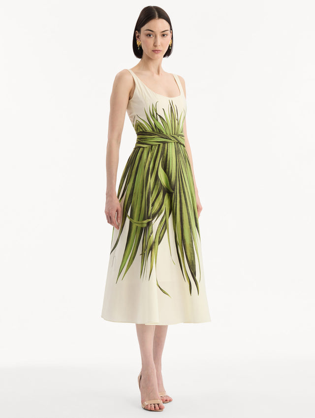 The model is wearing the Palm Leaves Cotton Poplin Dress. Featuring a scoop neckline, tank straps, cinched waist, and midi length. Side View.