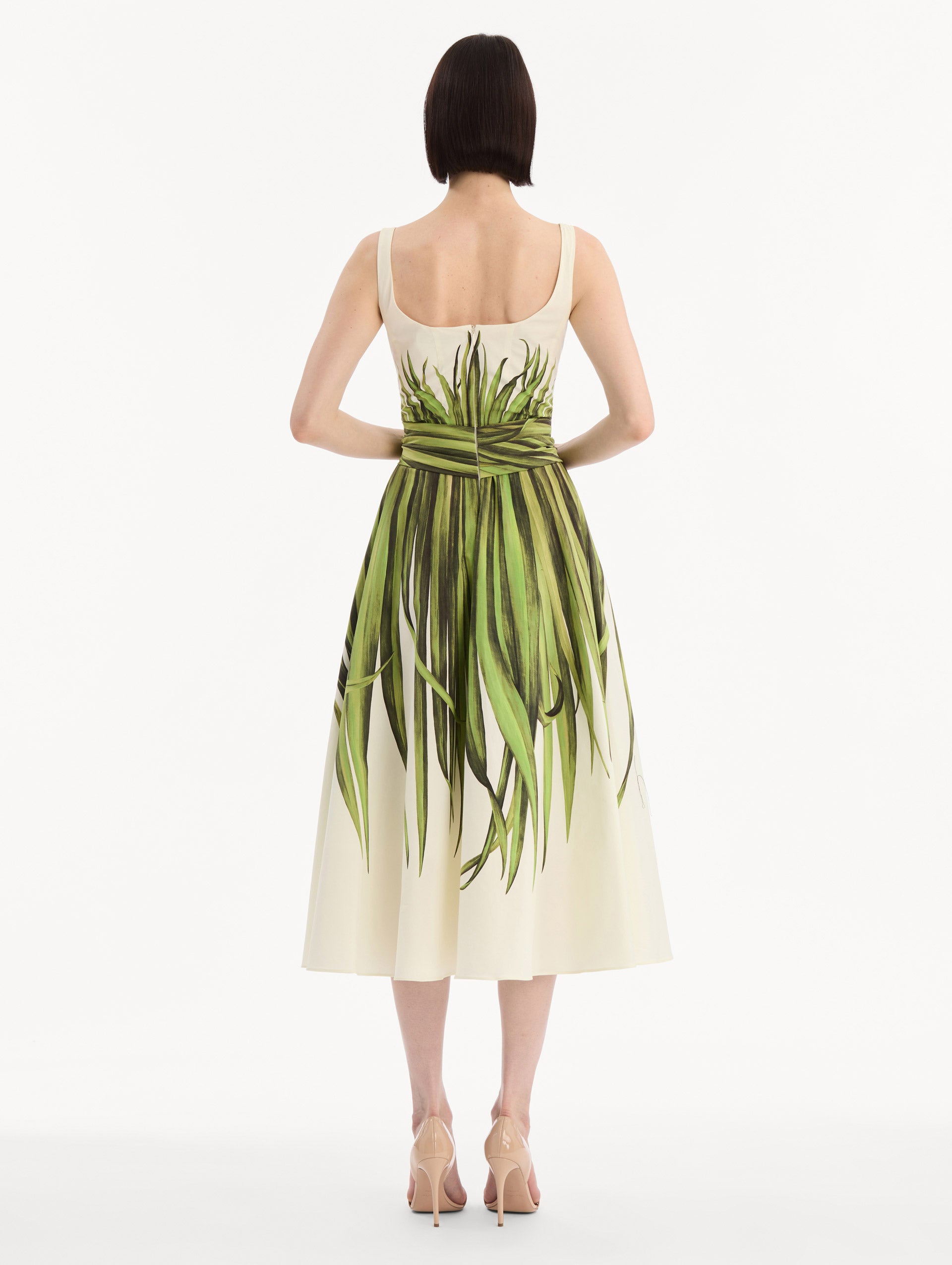 The model is wearing the Palm Leaves Cotton Poplin Dress. Featuring a scoop neckline, tank straps, cinched waist, and midi length. Back View.