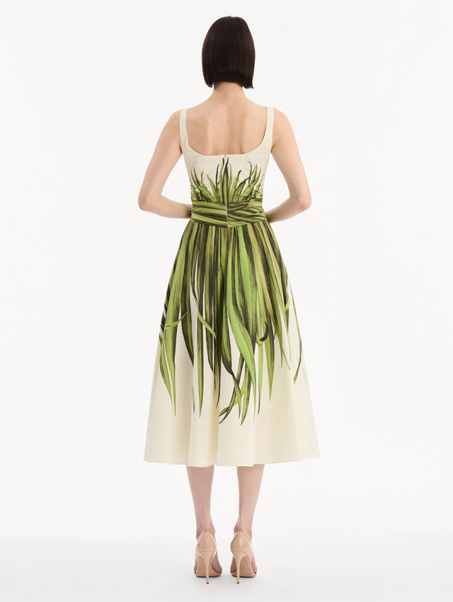 The model is wearing the Palm Leaves Cotton Poplin Dress. Featuring a scoop neckline, tank straps, cinched waist, and midi length. Back View.