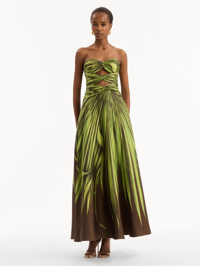 The model is wearing the Palm Leaves Silk Twill Cocktail Dress. Featuring a strapless silhouette, subtle cut-outs at the bodice, and a long skirt. Front View.