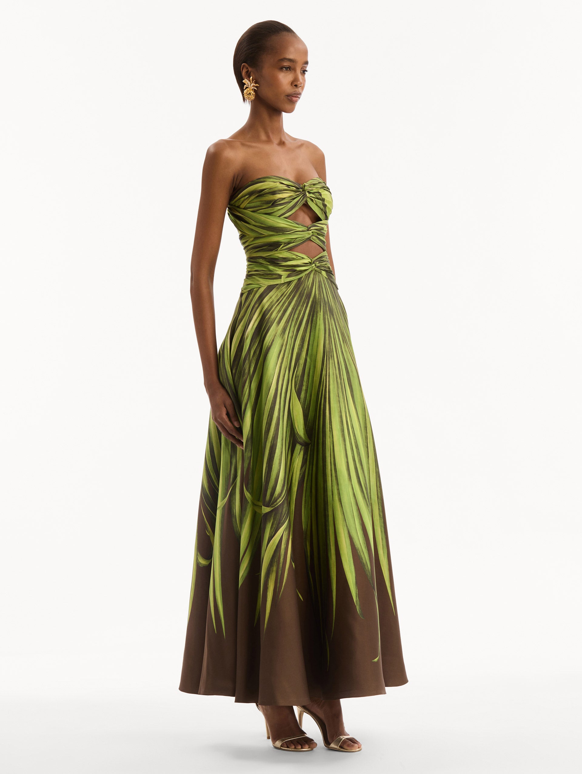 The model is wearing the Palm Leaves Silk Twill Cocktail Dress. Featuring a strapless silhouette, subtle cut-outs at the bodice, and a long skirt. Side View.