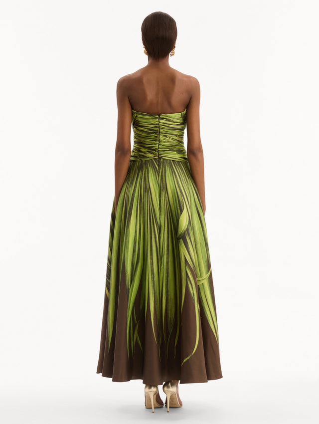 The model is wearing the Palm Leaves Silk Twill Cocktail Dress. Featuring a strapless silhouette, subtle cut-outs at the bodice, and a long skirt. Back View.