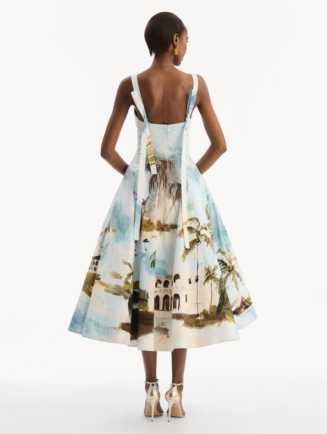 The model is wearing the Dominican Landscape Cotton Poplin Sleeveless Dress. Featuring tank straps with bow feature in back, and a full, midi-length skirt. Back View.